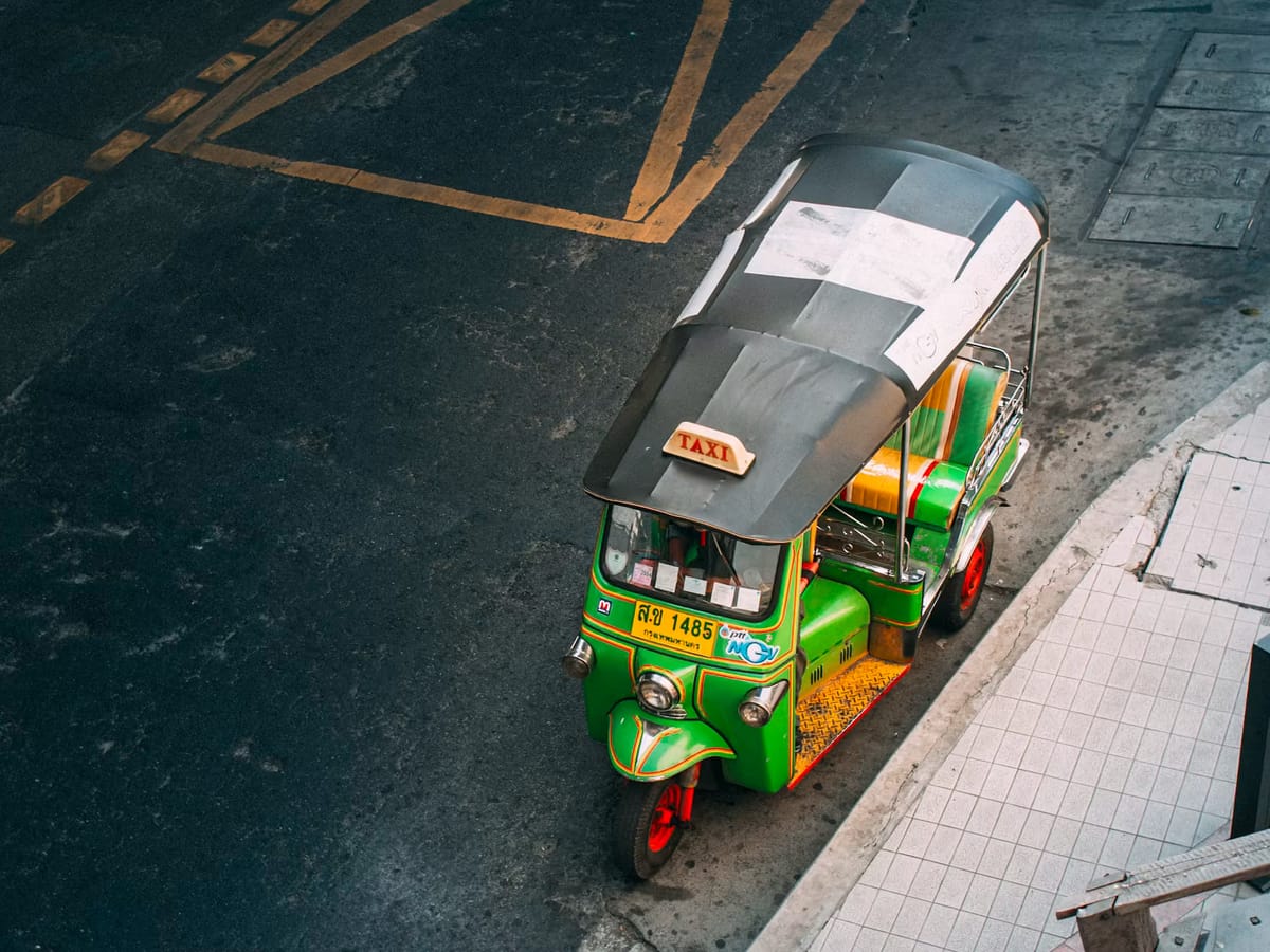 Green and yellow three-wheeler taxi parked by a road